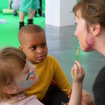 Facilitator Katriona Beales having her face painted by two children, at one of Autograph's Free Family SEND Workshops