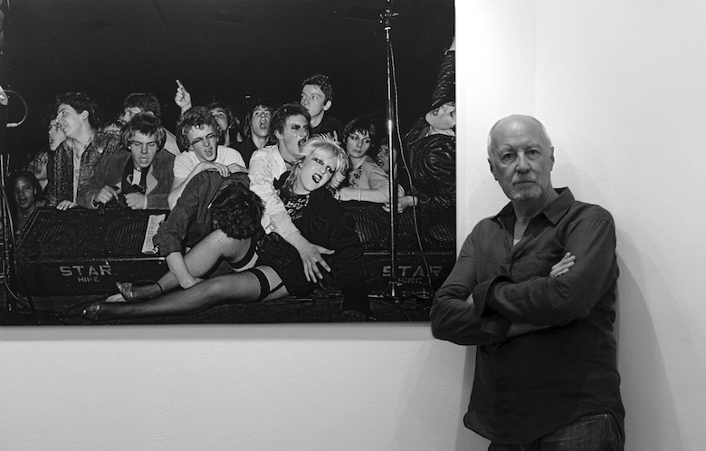 Photographer Syd Shelton stood in front photographs from Autograph's Rock Against Racism exhibition.